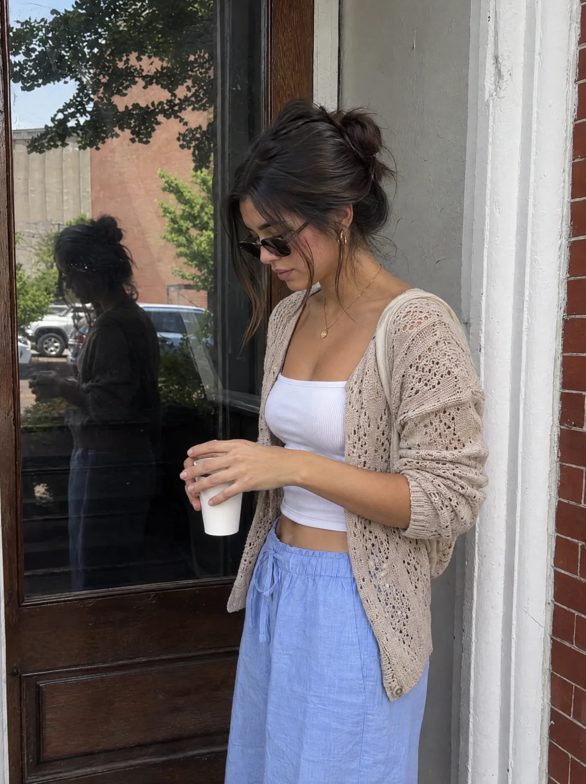 Eine Frau steht mit einem Kaffee vor einem Schaufenster.