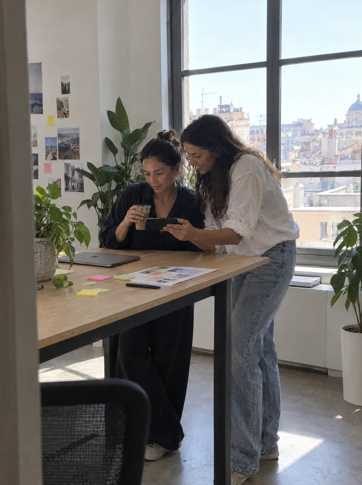Zwei Frauen betrachten gemeinsam ein Smartphone an einem Arbeitstisch.