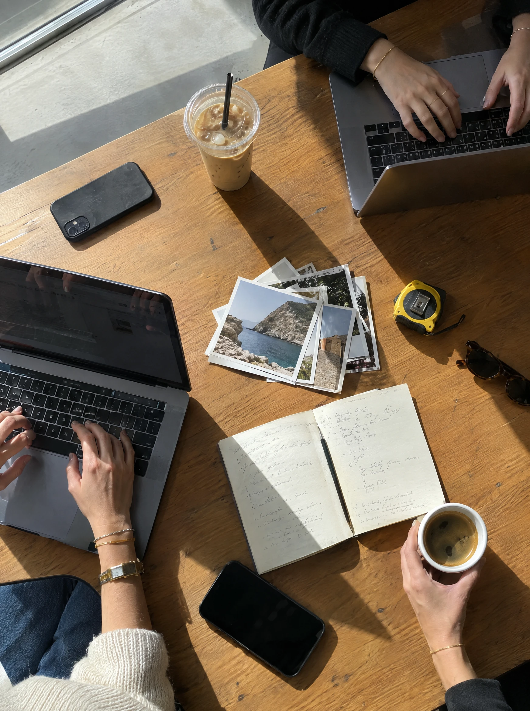Laptops, Fotos und Notizen liegen auf einem gemeinsamen Arbeitstisch.